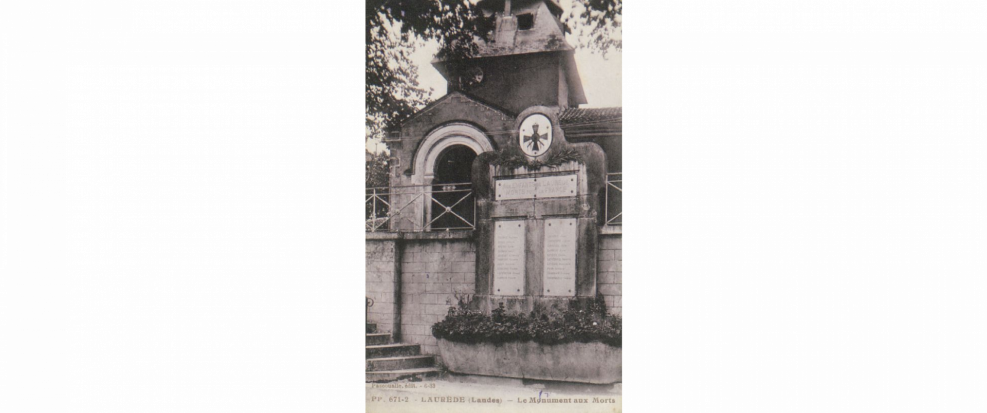 Photo en noir et blanc du monument aux morts. Il est adossé au mur qui borde la route de Poyanne.